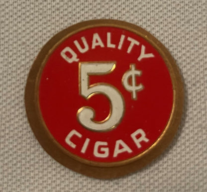 Round red and cream embossed metal token with "QUALITY 5¢ CIGAR" text and gold-colored border, photographed flat against beig
