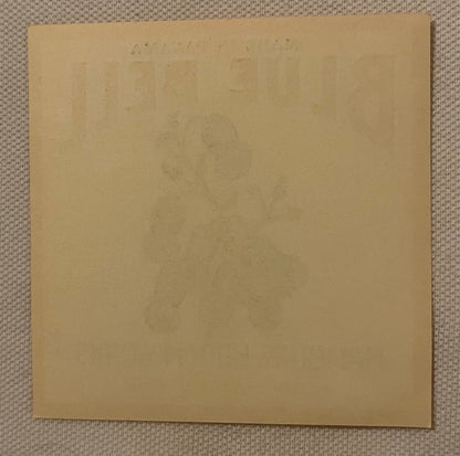 Blank tan cardboard sheet on textured beige fabric background, faint text visible at top edge