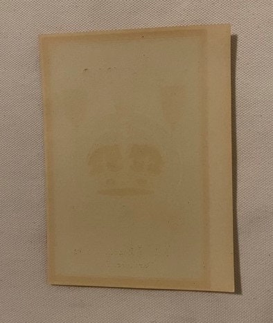 Cream-colored rectangular broom label with faint embossed circular design, displayed at angle against textured beige backgrou