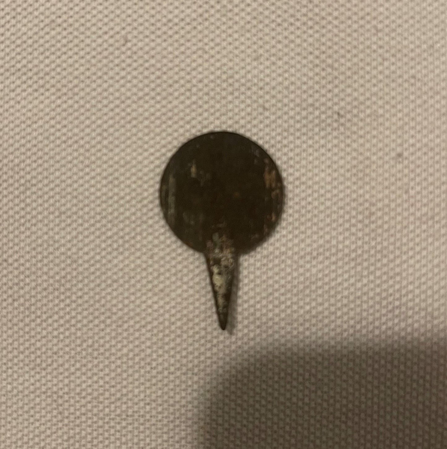 Antique metal pin tack with dark circular head and pointed stem on beige textured fabric background