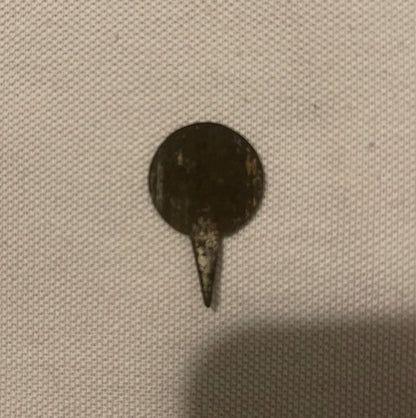 Antique metal pin tack with dark circular head and pointed stem on beige textured fabric background
