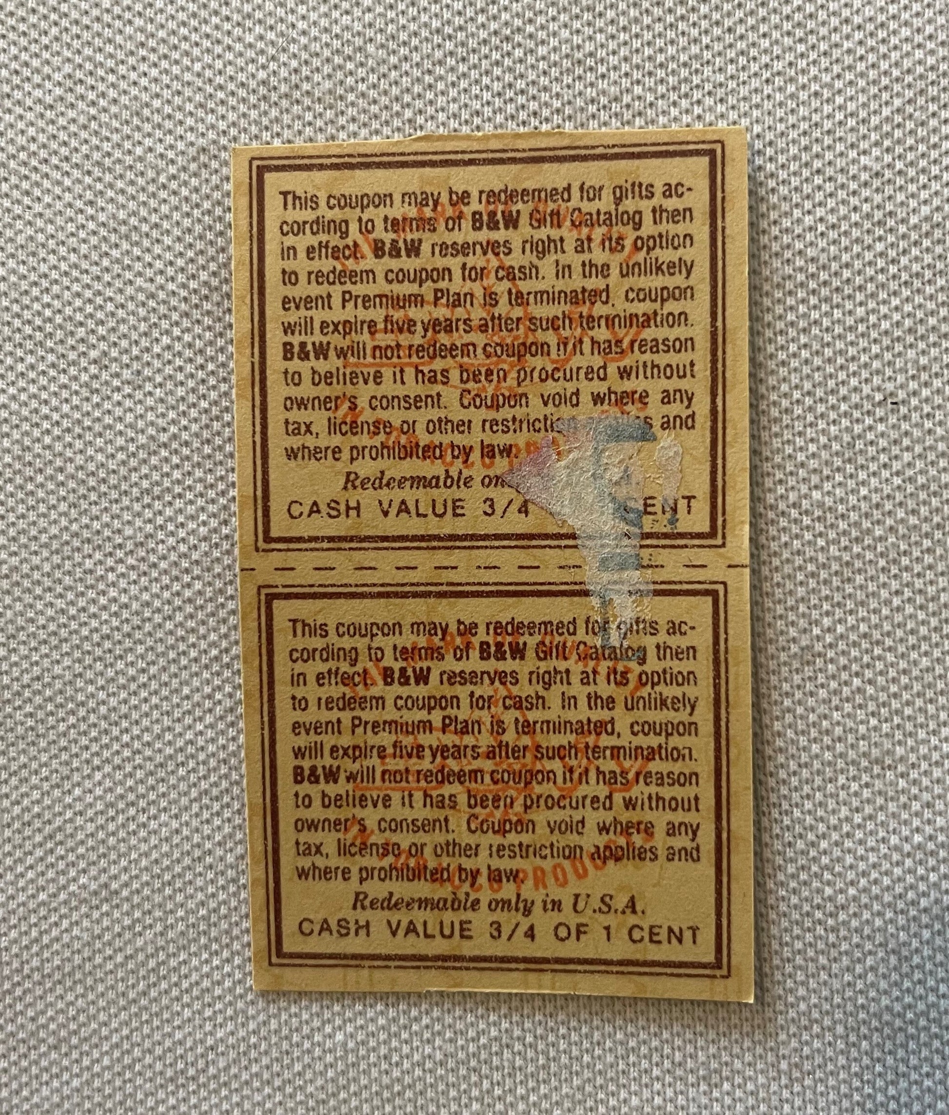 Two tan vintage B&W tobacco coupons with printed terms and 3/4 cent cash value, perforated at center, photographed flat on gr