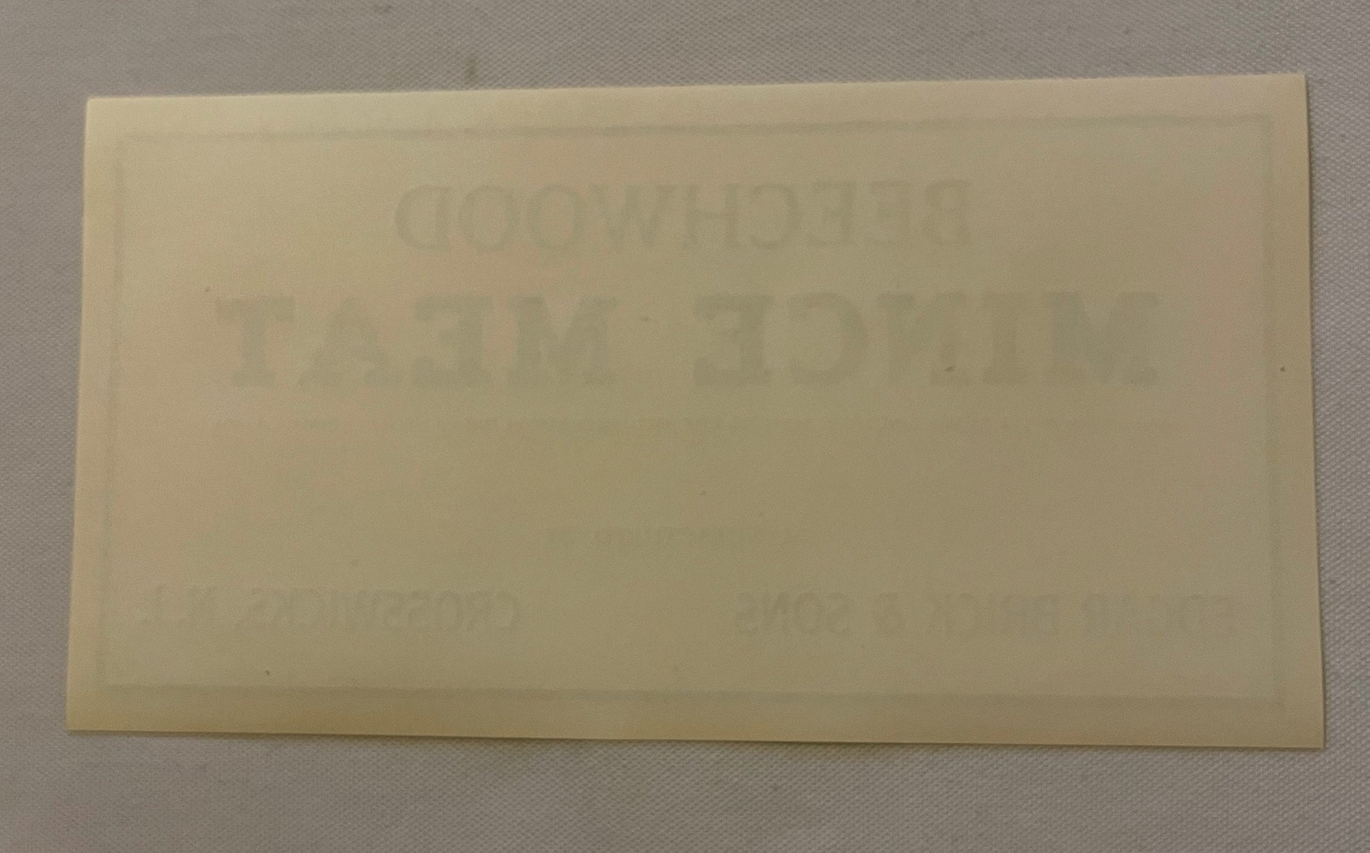Cream-colored rectangular beechwood label with faint embossed text, photographed flat against light gray background