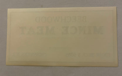 Cream-colored rectangular beechwood label with faint embossed text, photographed flat against light gray background