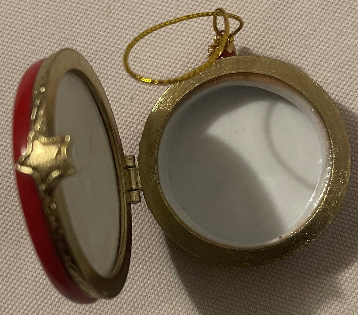 The peace sign trinket box ornament open on its gold-tone hinge: the red and white porcelain lid and the white porcelain well inside, gold cord loop above