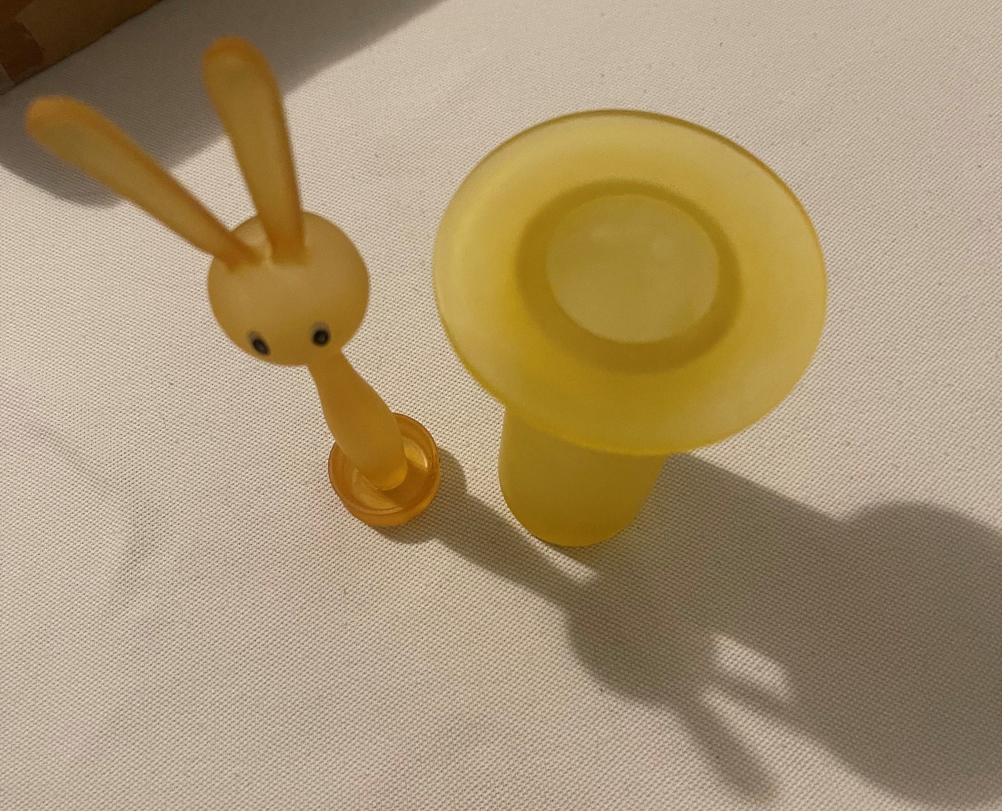 Amber yellow glass bunny toothpick holder photographed from above on white fabric, showing rabbit figurine with long ears and