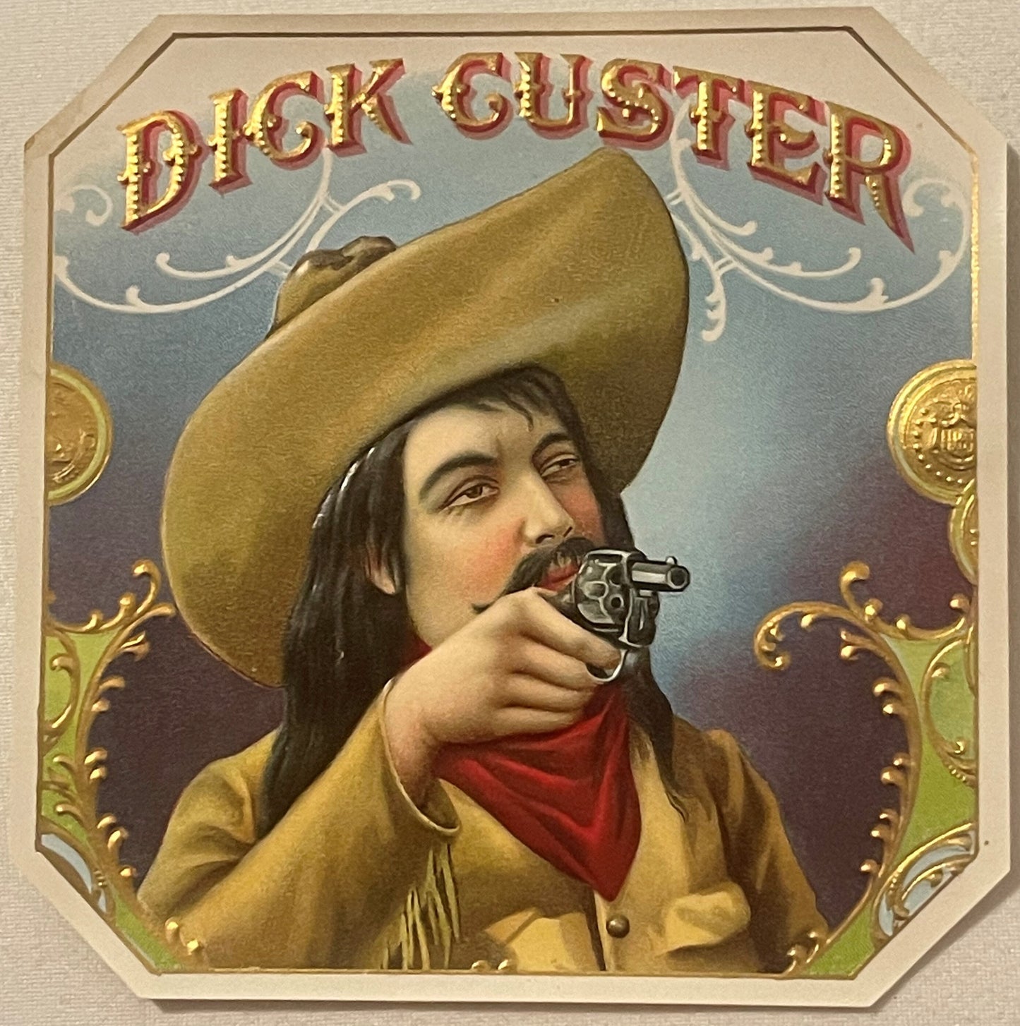 Gold embossed chromolithograph cigar label featuring a cowboy in tan hat and jacket with red bandana, aiming a revolver, "Dic