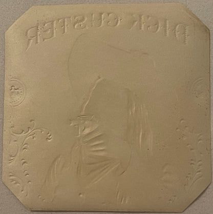 Cream-colored embossed label with cowboy profile in center, decorative corner flourishes, and text reading "Dick Custer" at t