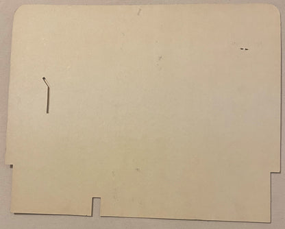 Cream-colored cardboard die-cut display sign with rectangular cutouts and a bent metal tab, shown flat against textured