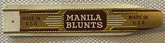 Gilt gold embossed cigar band with "Manila Blunts" text and "Made in U.S.A." on either side, photographed flat against woven 
