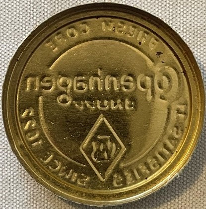 Round brass tin lid with embossed text reading "It Satisfies Since 1822" and a diamond-shaped symbol, photographed from above
