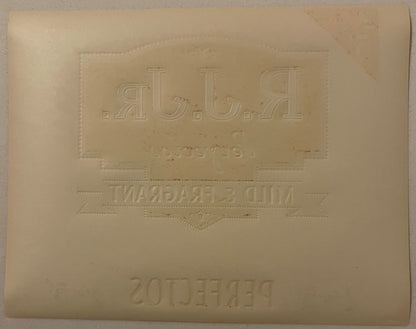 Reverse of the R.J. Jr. Perfectos label: blank cream paper with the blind-embossed mirror-image of the front panel - backward R.J.JR., Mild & Fragrant, and Perfectos lettering, with scattered ink offset marks, no color.