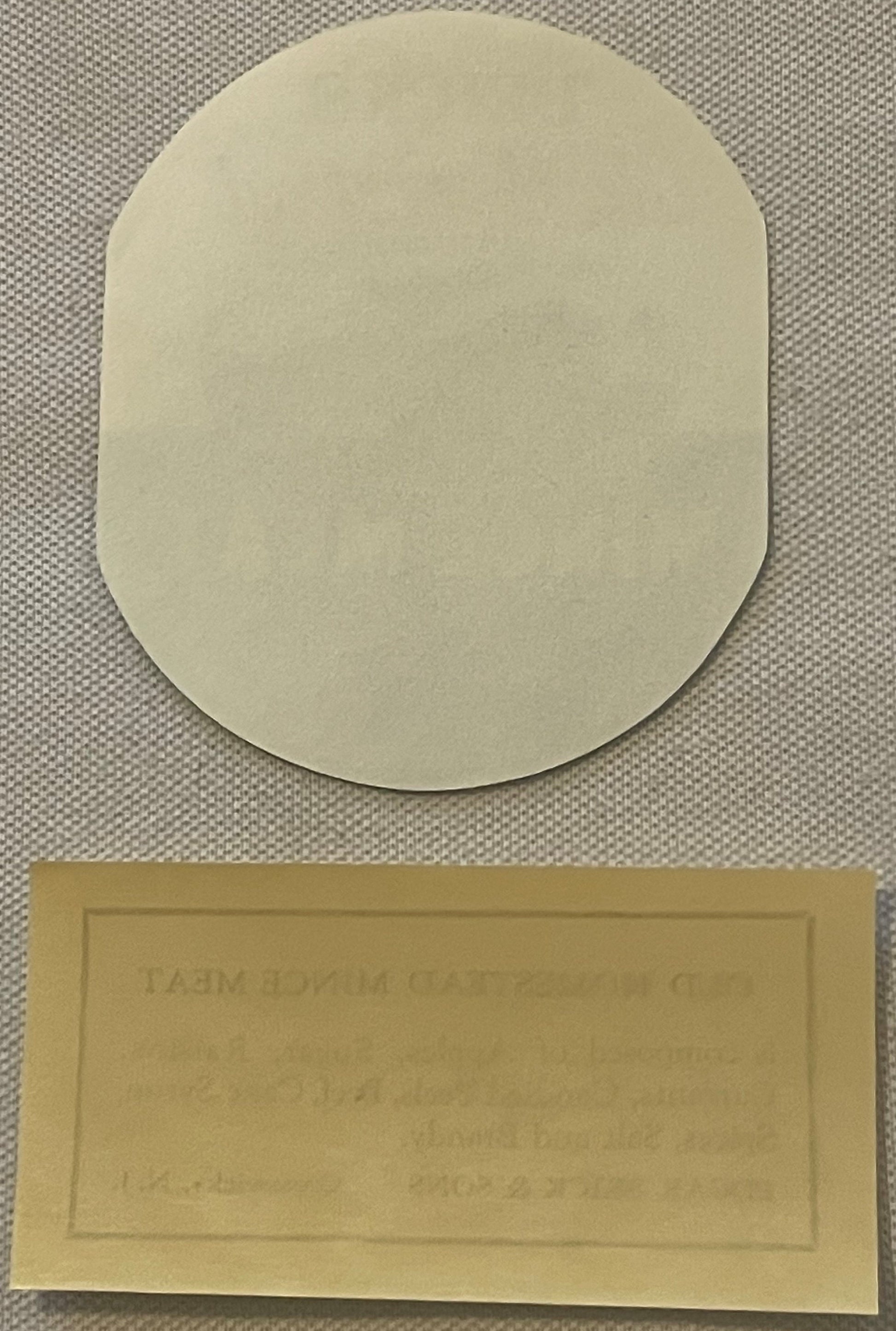 Two cream-colored vintage labels on textured fabric background; top label is rounded rectangle, bottom label is rectangular w