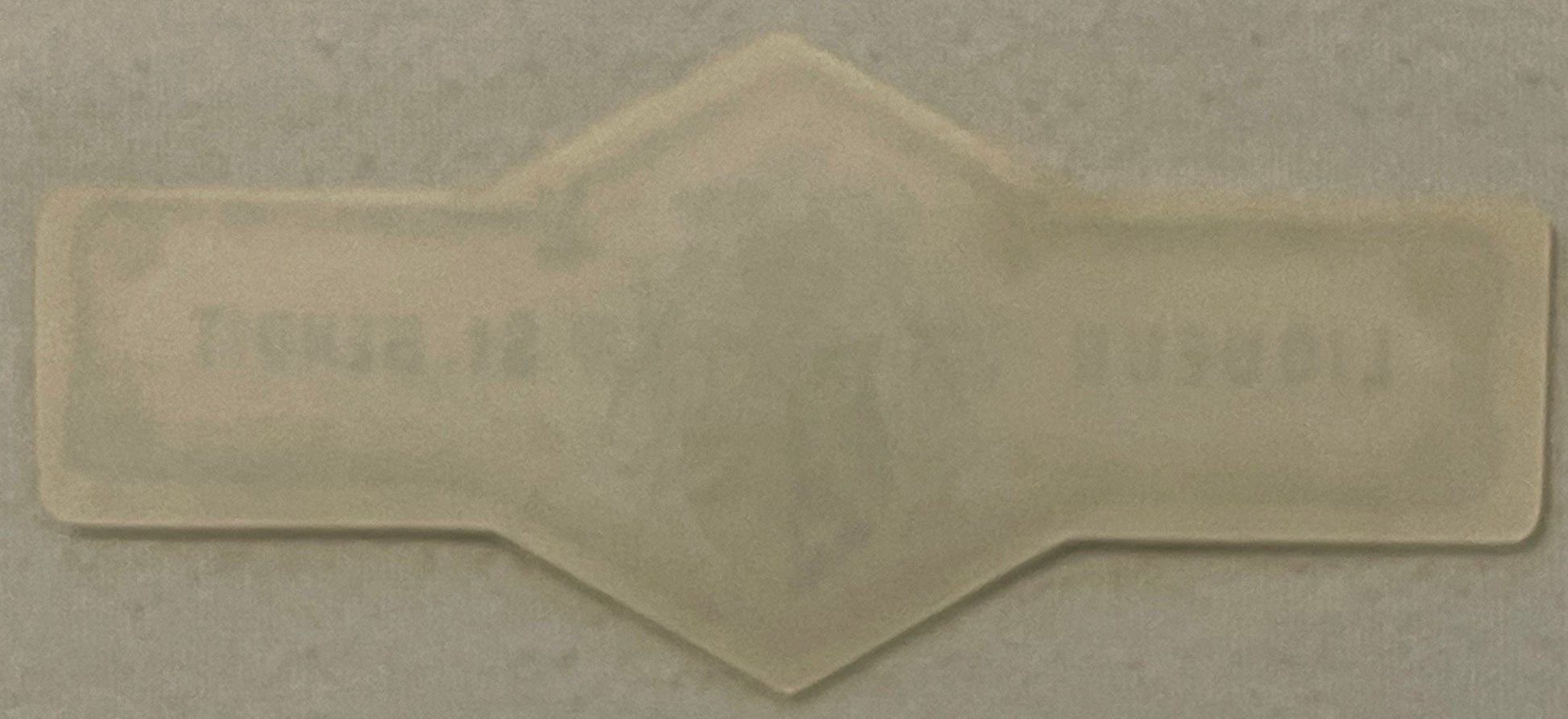 Translucent white embossed neck label with symmetrical curved design and central heraldic crest, photographed against light b