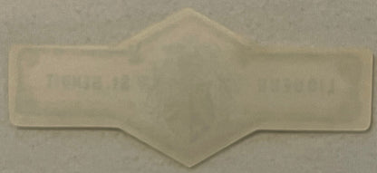Translucent white embossed neck label with symmetrical curved design and central heraldic crest, photographed against light b