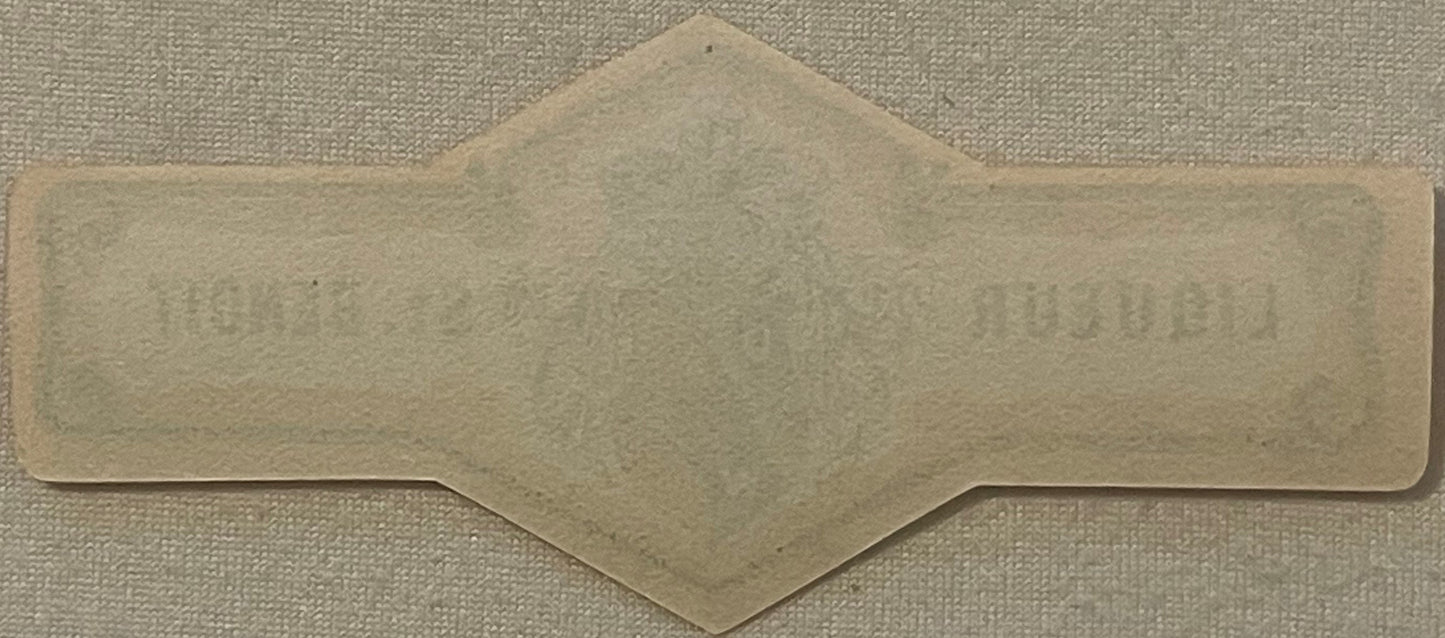 Blank cream-colored vintage bottle neck label with decorative scalloped edges and pointed top, photographed flat on textured 