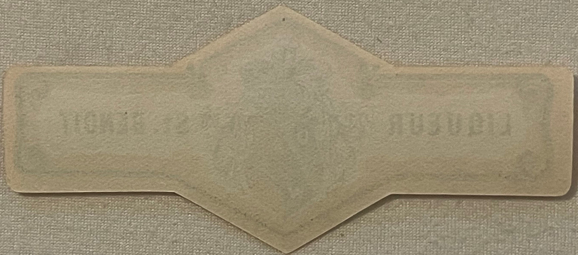 Blank cream-colored vintage bottle neck label with decorative scalloped edges and pointed top, photographed flat on textured 