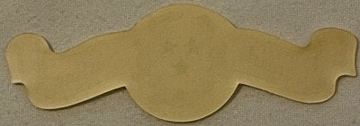 Tan die-cut paper collar label with wavy edges and scalloped side wings, displayed flat on neutral fabric background