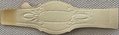 Cream-colored embossed cigar band with ornate floral scrollwork and central oval cartouche, displayed flat against textured f