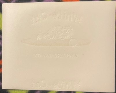 Cream-colored embossed cigar box label with faint gold chromolithograph design and text, shown flat against colorful backgrou