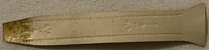 Gold foil embossed cigar band with tapered rectangular shape on beige fabric background, showing ornate lettering and decorat