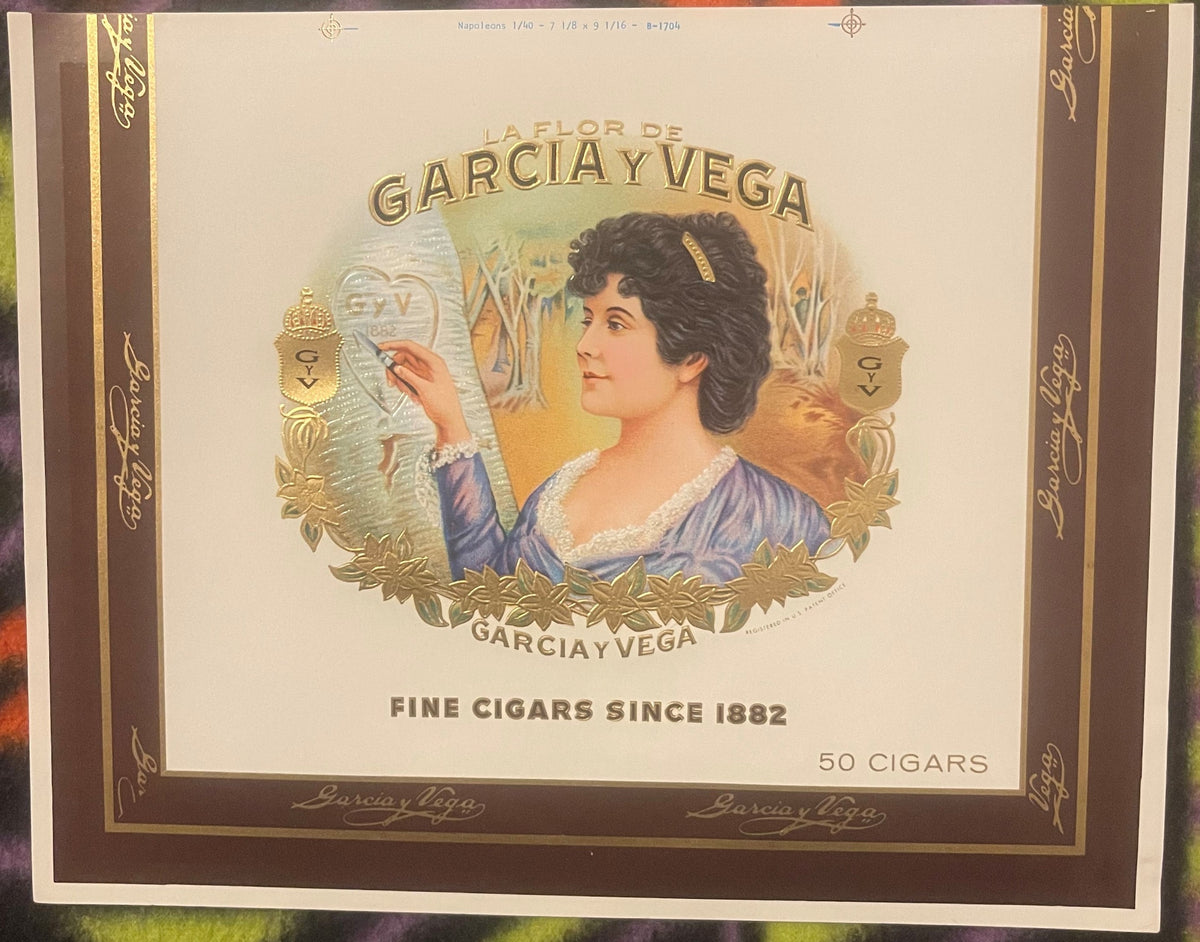 Vintage cigar box label featuring a woman in profile wearing blue dress with gold foil embossed border and text "La Flor de G