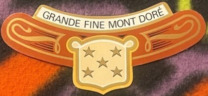 Ornate vintage wine label with orange scrollwork, gold shield bearing five stars, and banner reading "GRANDE FINE MONT DORÉ