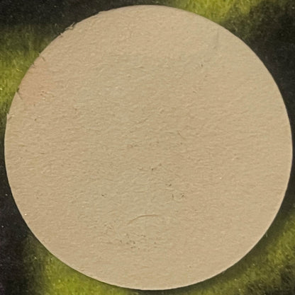 Cream-colored circular wine barrel label on green fabric background, blank face with subtle texture visible