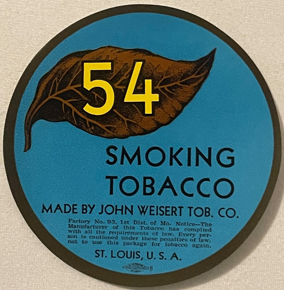 Circular blue tobacco label with brown leaf illustration, yellow "54" text, and "Smoking Tobacco" printed below, made by John