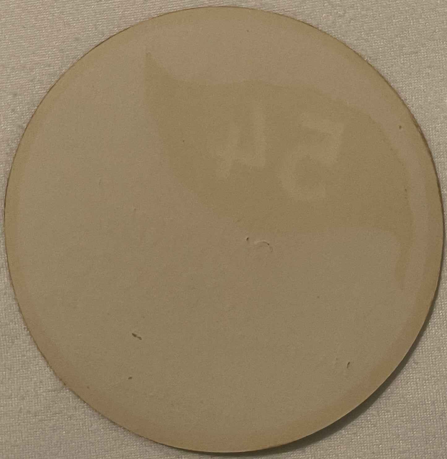 Blank cream-colored circular tobacco label on textured beige fabric background, showing wear marks and slight discoloration