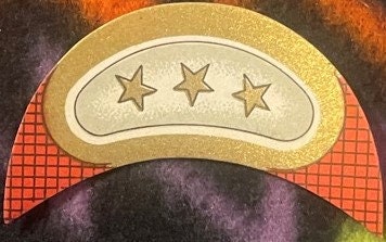 Embossed gold wine label with three stars in crescent shape, cream-colored, displayed against colorful textured background