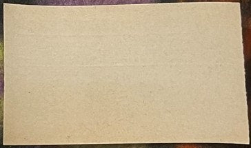 Blank cream-colored antique pharmacy label on purple fabric background, showing age spots and wear