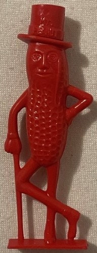 Vintage red plastic Mr. Peanut figural whistle with top hat and monocle, shown standing against neutral fabric background