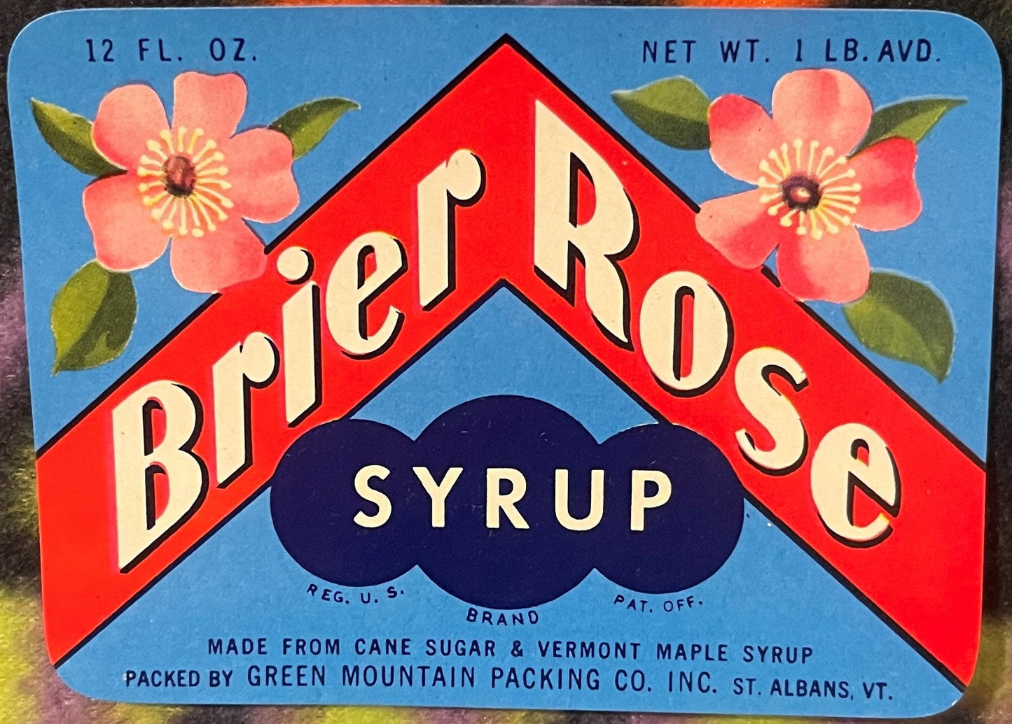 Vintage Brier Rose syrup label with red chevron design, pink flowers, blue background, and dark cloud banner reading "SYRUP