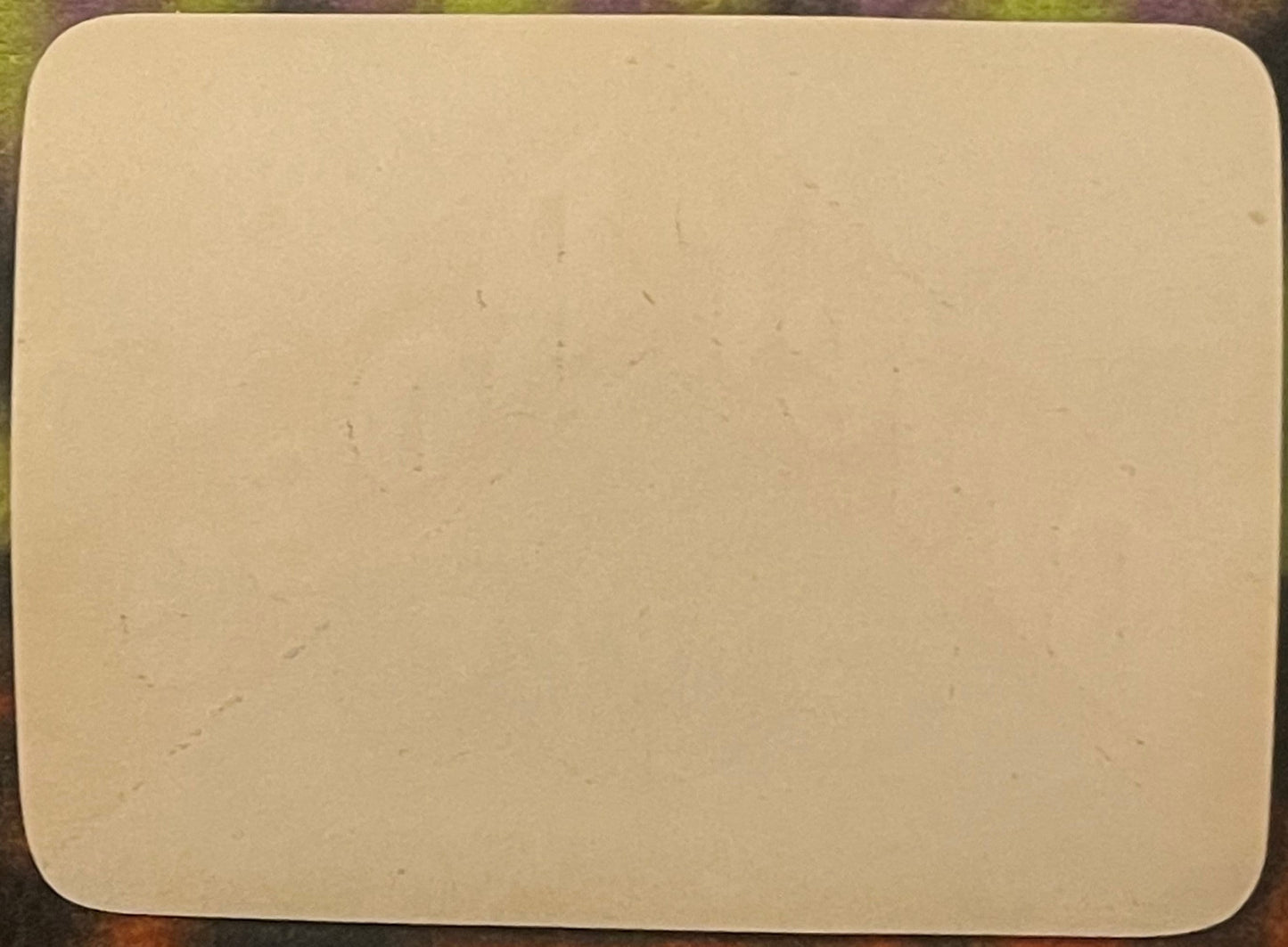 Blank cream-colored rectangular label with rounded corners on green fabric background, showing age spots and slight wear