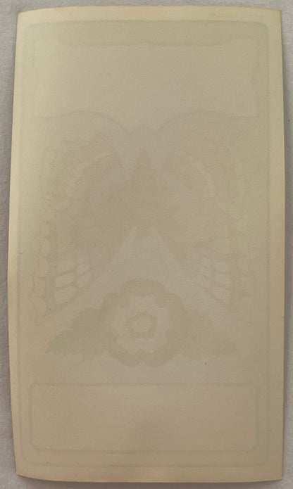 Cream-colored blank label with faint embossed butterfly and decorative border design, photographed flat against gray surface
