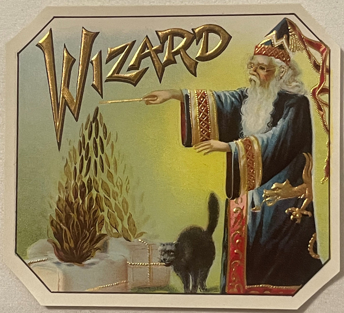 Antique gold-embossed cigar box label featuring a wizard in blue robes pointing a wand at flames and a black cat, with ornate