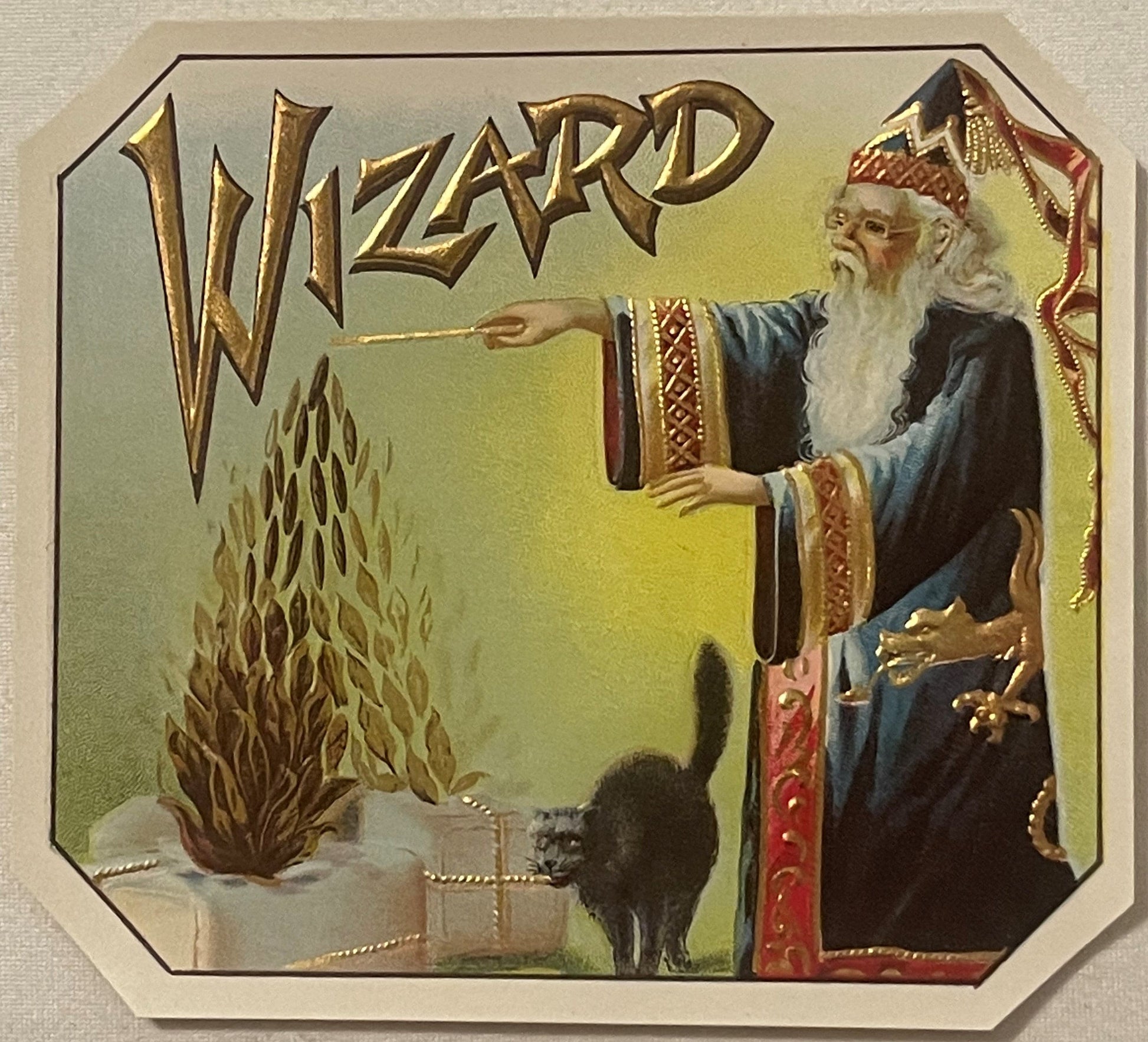 Antique gold-embossed cigar box label featuring a wizard in blue robes pointing a wand at flames and a black cat, with ornate