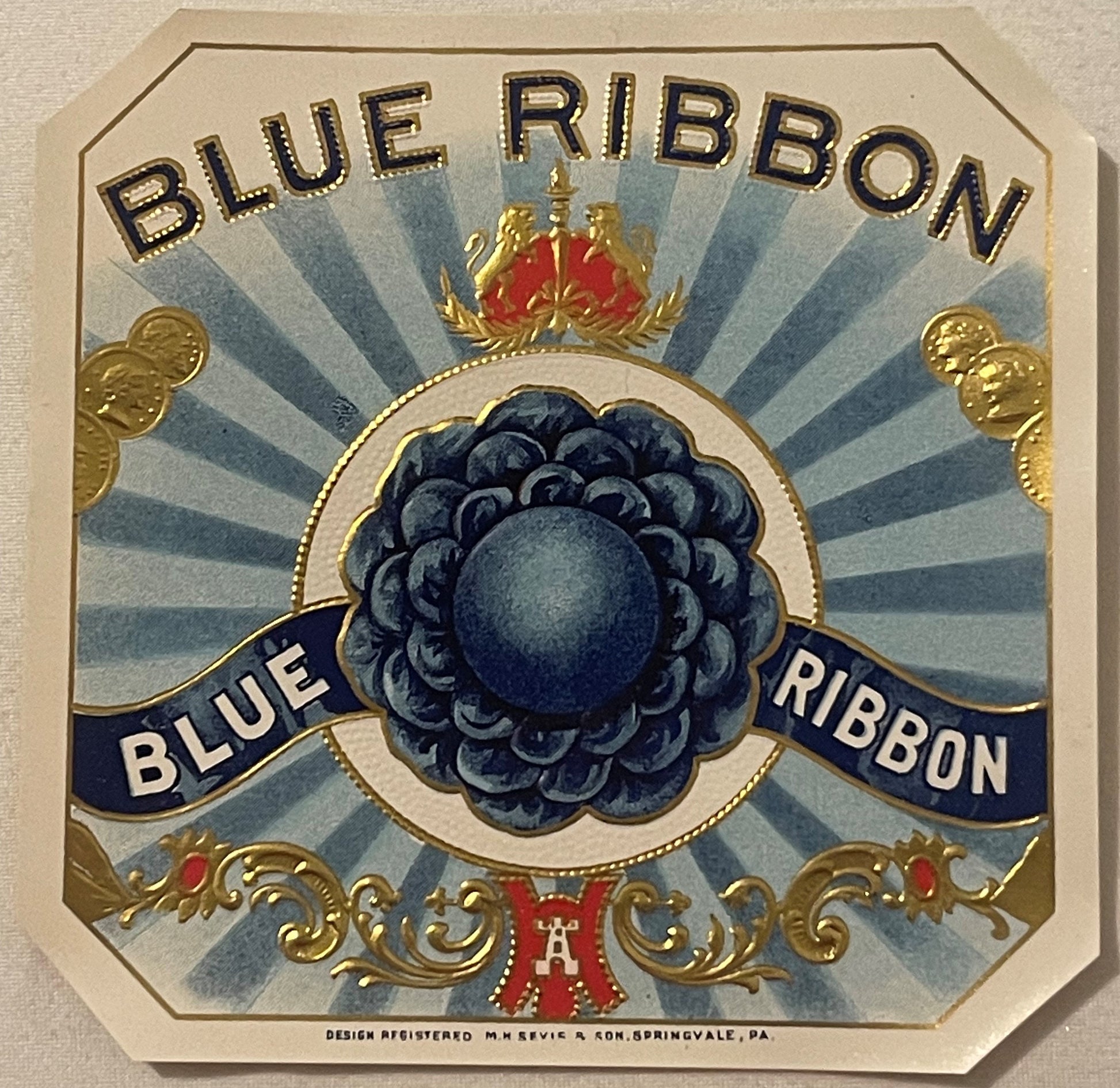 Antique gold-embossed cigar box label featuring "Blue Ribbon" text, central blue berry cluster, crown, and decorative scrollw