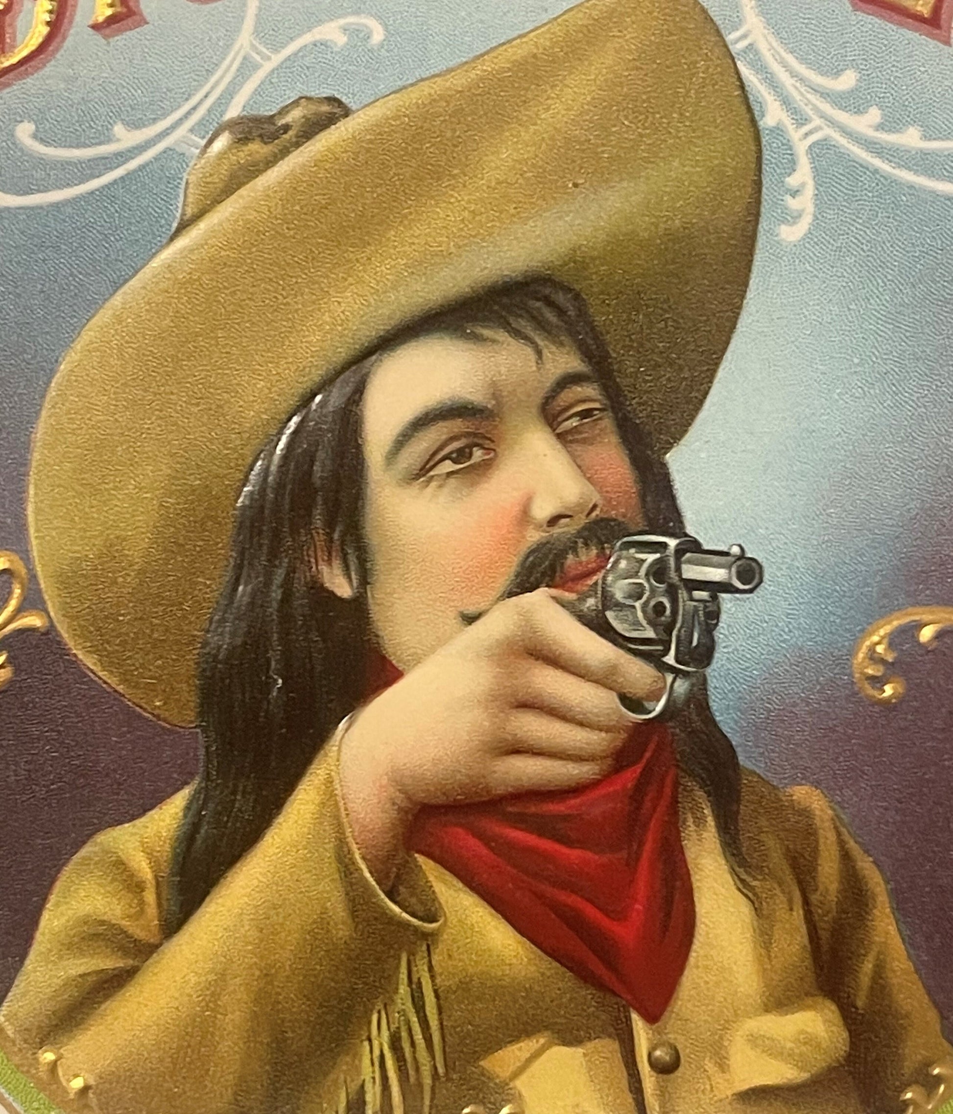 Gold embossed chromolithograph cigar label featuring a cowboy with long dark hair and mustache wearing a tan jacket, red band
