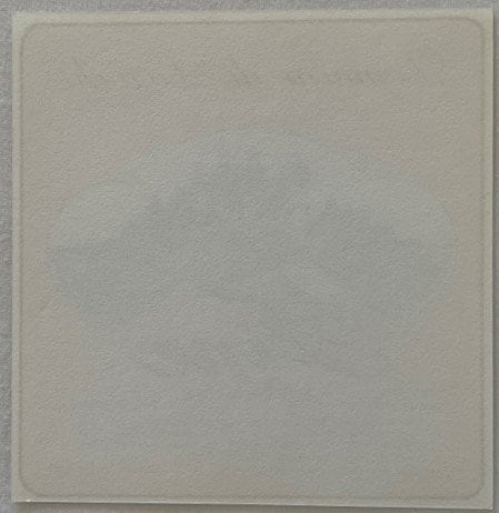 Blank cream-colored square label or paper against gray background, appears unused or back side of vintage spirit label