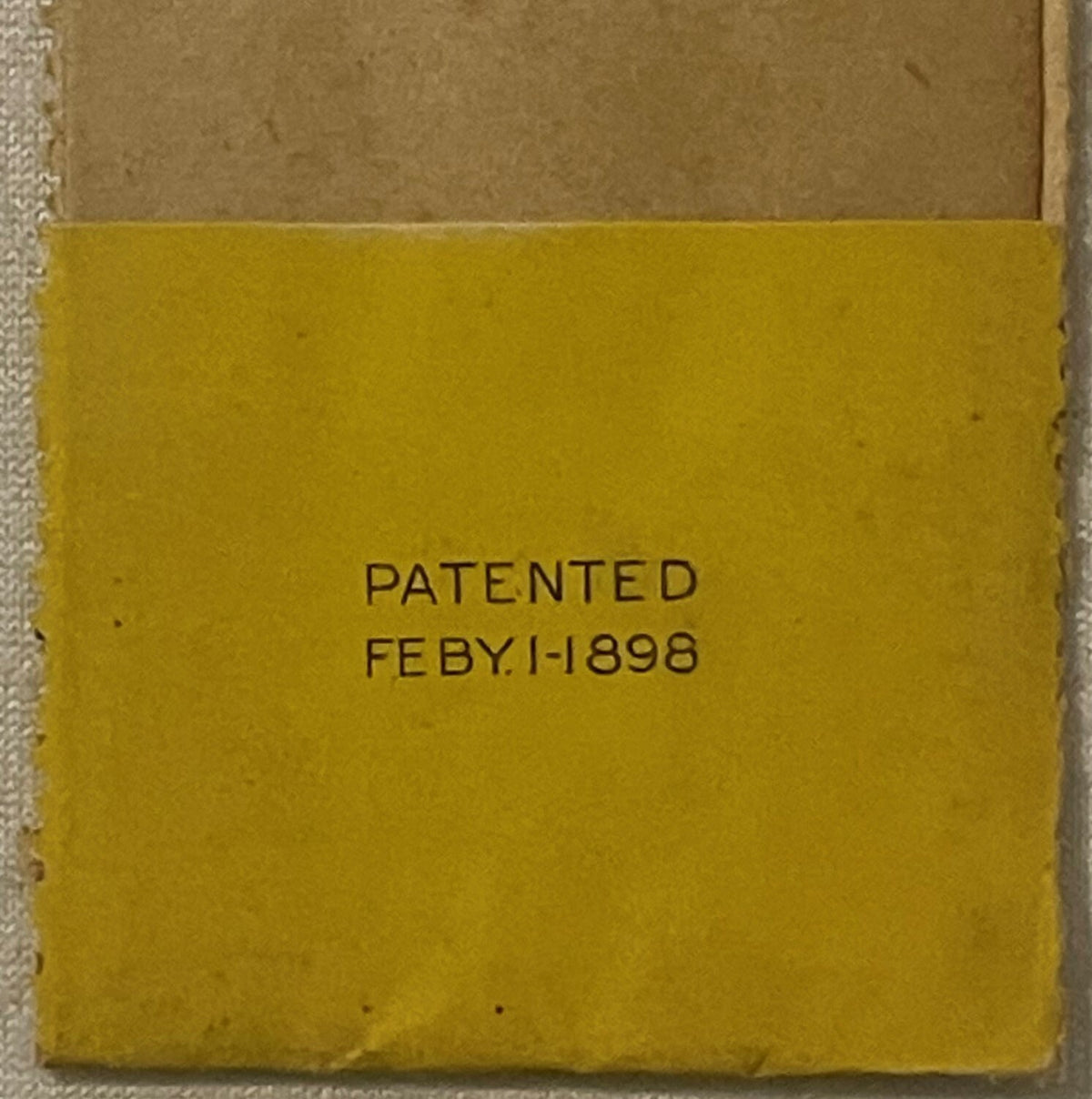 Yellow vintage label with "PATENTED FEBY.1-1898" embossed text, tan cardboard visible above, shown flat against white surface