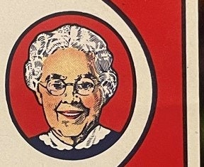 Vintage soda label featuring a smiling elderly woman with white hair and glasses in a circular portrait on red background