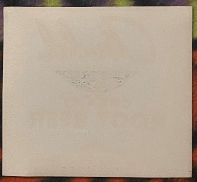 Blank cream-colored paper or label backing with faint pencil marks, photographed flat against a colorful fabric background