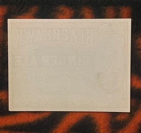 Blank cream-colored vintage label on dark patterned fabric background for scale