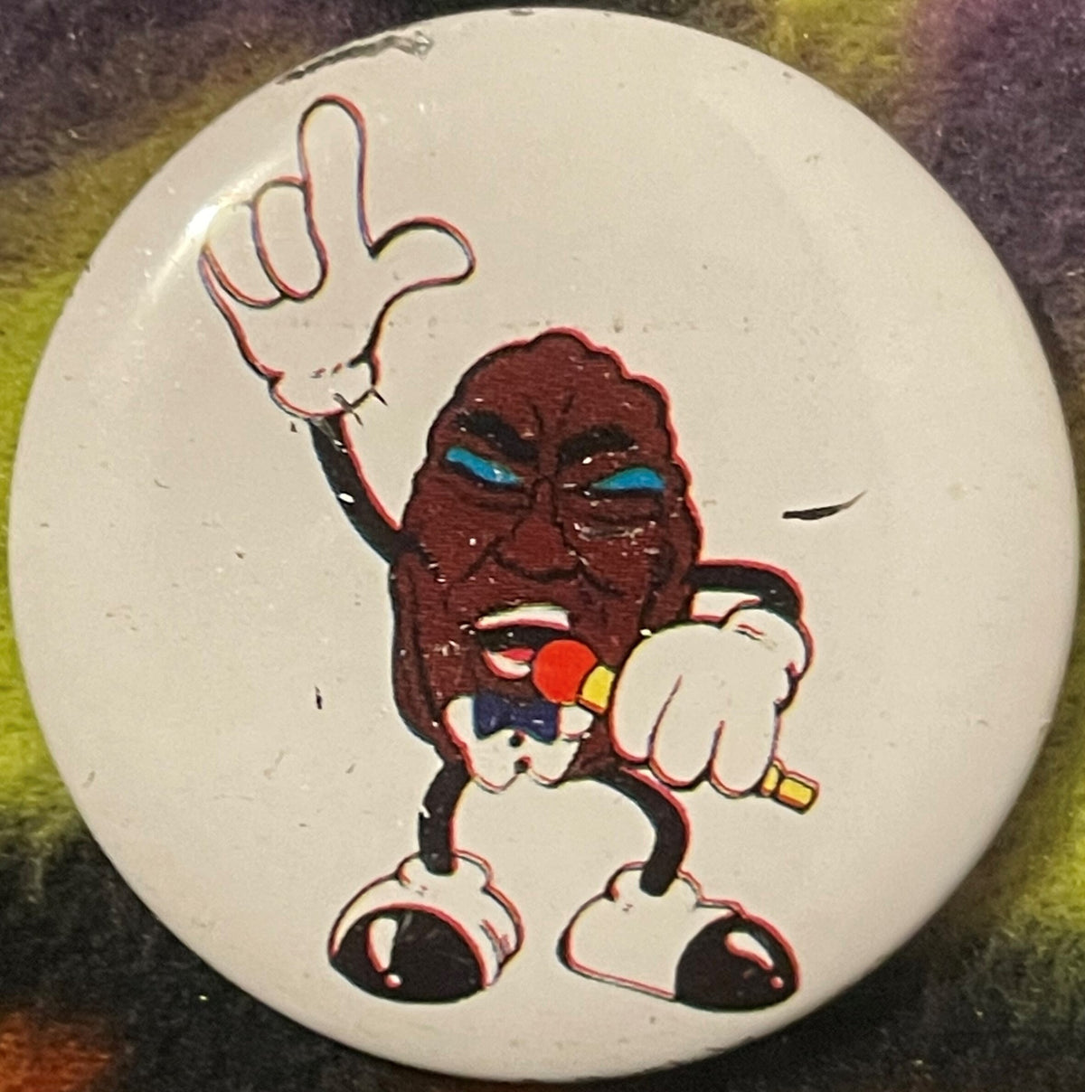 Single cream-colored pinback button featuring a brown raisin character with blue eyes, white gloves, and red nose holding a m