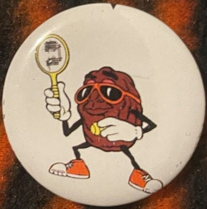 Vintage pin featuring anthropomorphic raisin character in sunglasses and red cap holding tennis racket, on cream-colored