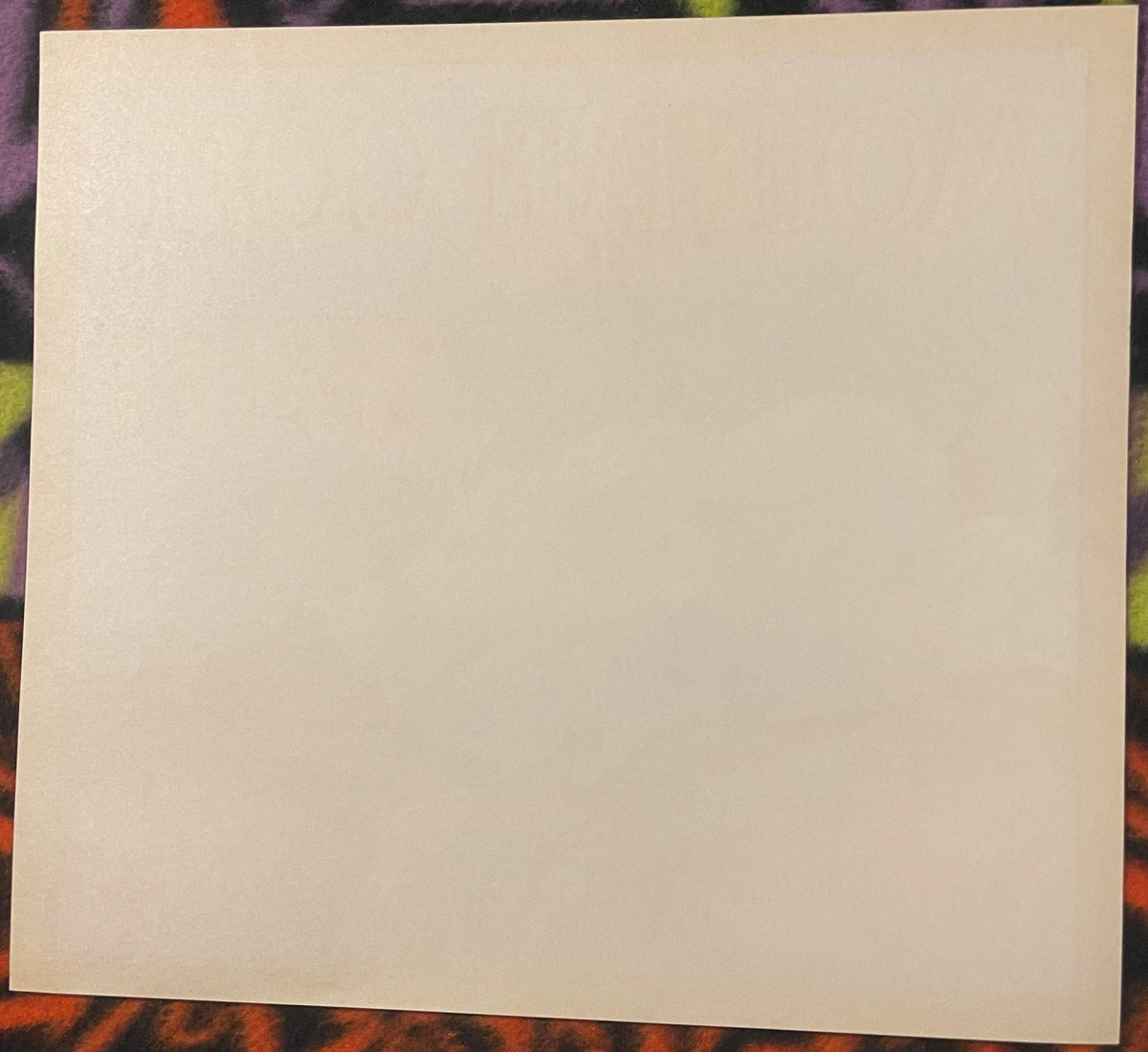 Plain cream back of the Mountain Goat apple crate label, the front lettering showing faintly through, laid on patterned cloth.