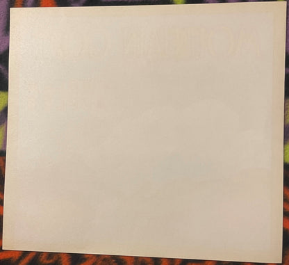 Plain cream back of the Mountain Goat apple crate label, the front lettering showing faintly through, laid on patterned cloth.