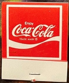 Vintage Coca-Cola matchbook with red cover featuring white "Enjoy Coca-Cola" logo and cream-colored striking strip at bottom